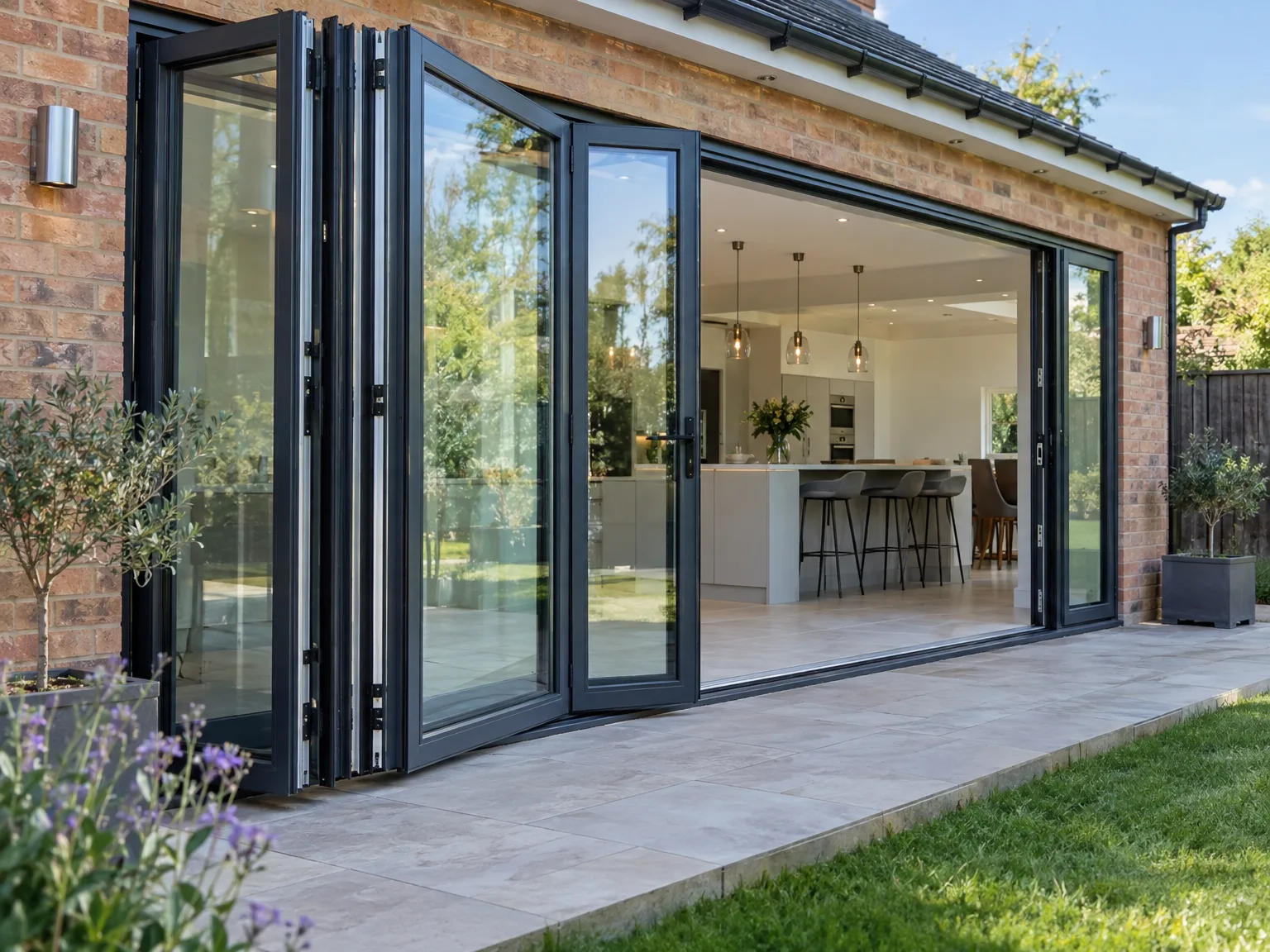 Black bifold doors opening onto stone patio with landscaping and lawn area