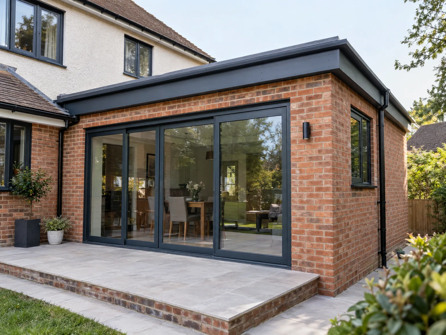 Brick house extension with black bifold doors opening onto paved patio area