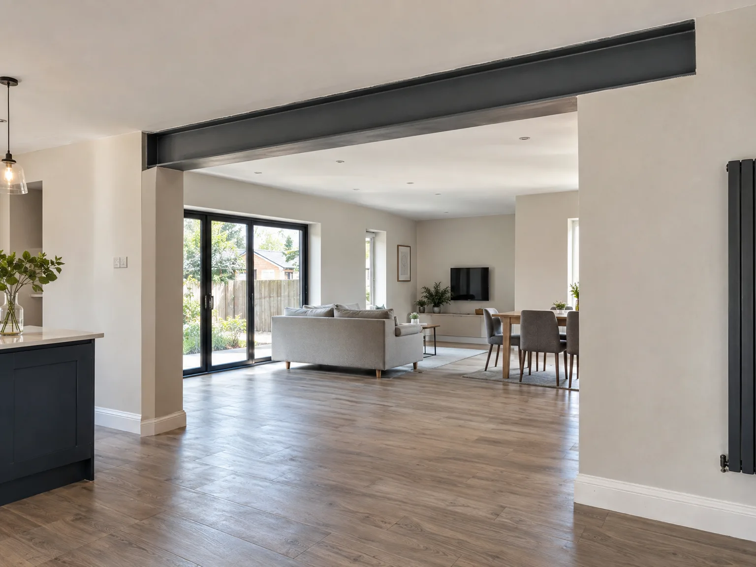 Open-plan house extension with black structural beam, wooden flooring, and bi-fold doors to garden